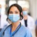 Close up face of confident female nurse in front of his medical staff looking at camera while wearing protective face mask due to covid-19 virus. Smiling surgeon standing  with team in background.