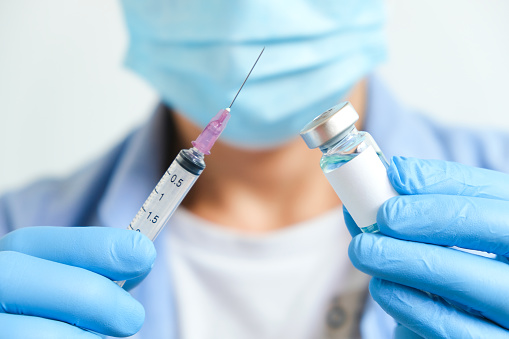 doctor's hand holds a syringe and a blue vaccine bottle at the hospital. Health and medical concepts.